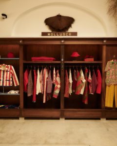 An open wardrobe made of dark brown wood neatly hung with clothes in warm red tones accented with white and yellow.