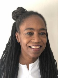 A portrait of a dark-skinned woman looking slightly off camera and smiling. She has long black hair and wears a white shirt.