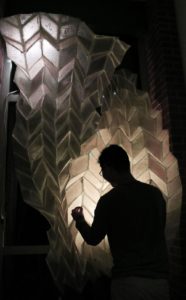 A black silhouette of an individual in front of a back-lit translucent sculpture with geometric shapes