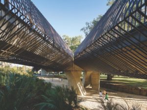 Crisscrossing concrete walkways encased in diamond-shaped metal cages tower on concrete pillars over the children running on the ground below.