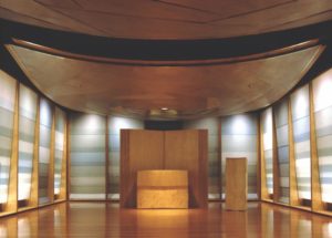 The symmetrical interior of a wood-paneled chapel, with the ceiling above the altar made of a single massive, curved piece of wood.