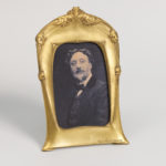A gold-toned standing vertical picture frame with an old photograph of a man.