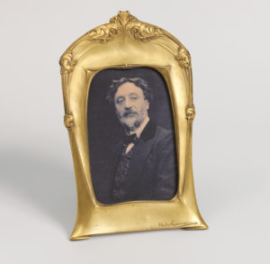 A gold-toned standing vertical picture frame with an old photograph of a man.