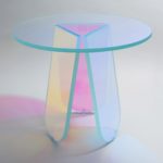 Glass table formed by a circular top on tripod base composed of three angled, oval legs. Glass iridizes and changes color depending on angle of view.