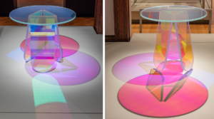 Side-by-side photographs of a glass table, with a round top and three board-shaped legs, seen from two angles: in one angle the table appears blue, green, and purple and casts pink, purple, and mint shadows; in the other angle the table appears pink, orange, and yellow and casts pink, purple, and orange shadows.