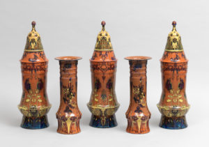 A collection of five burnt orange vases, each with unique ornamental designs in red, blue, and yellow.