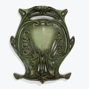 A dark green, cast iron medallion decorated with curving, symmetrical lines.