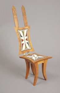 A wooden chair with curved legs and long wooden beams extending from the back. Embedded in both the seat and the chair back is a colorful, abstract pattern created with glass beads.