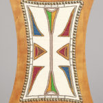 Close-up view of the back of a wooden chair, a rectangular shape with concave edges and, embedded into it on deer hide, glass beads in white, brown, blue, red, green, and orange forming graphic abstract shapes.