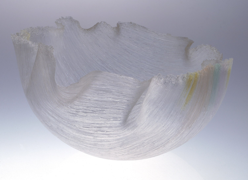 A sculptural, organically shaped glass bowl. The lip of the bowl undulates according to how the material set and the surface appears to have fine grooves created by the threads of glass that form the vessel’s structure.