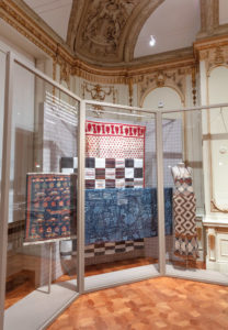 Several vibrantly colored and patterned textiles are displayed behind a glass case.