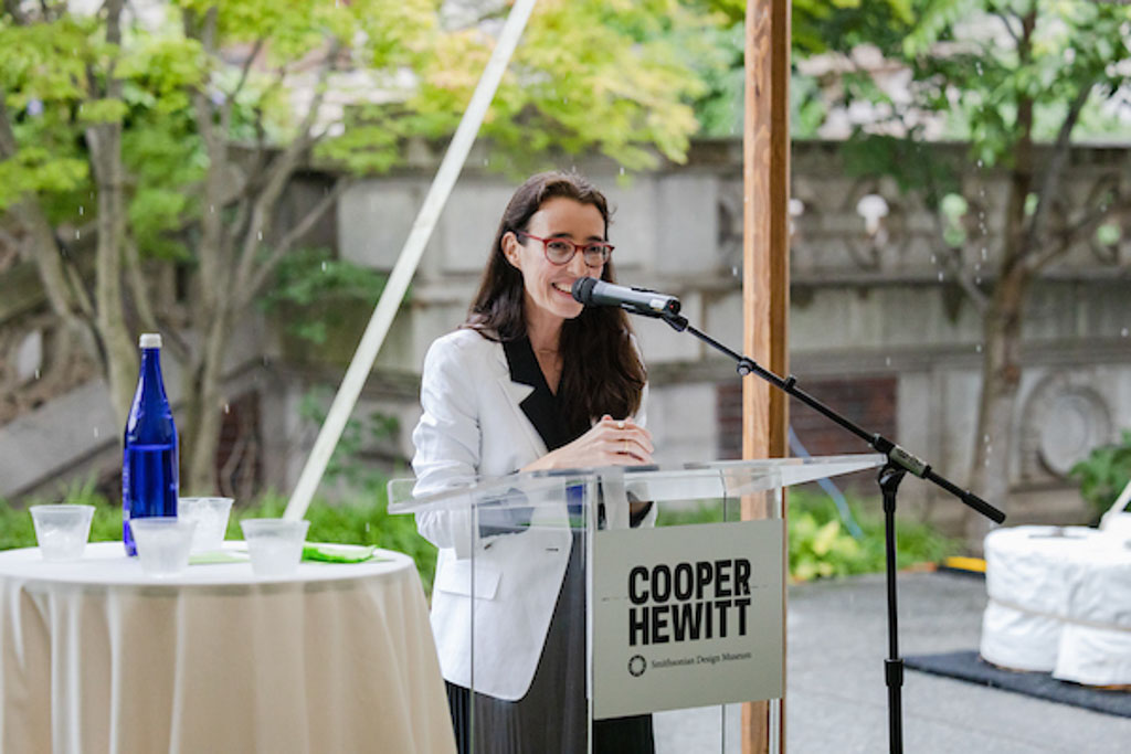 Cooper Hewitt Director Maria Nicanor smiles as she speaks at a podium beneath an outdoor tent.