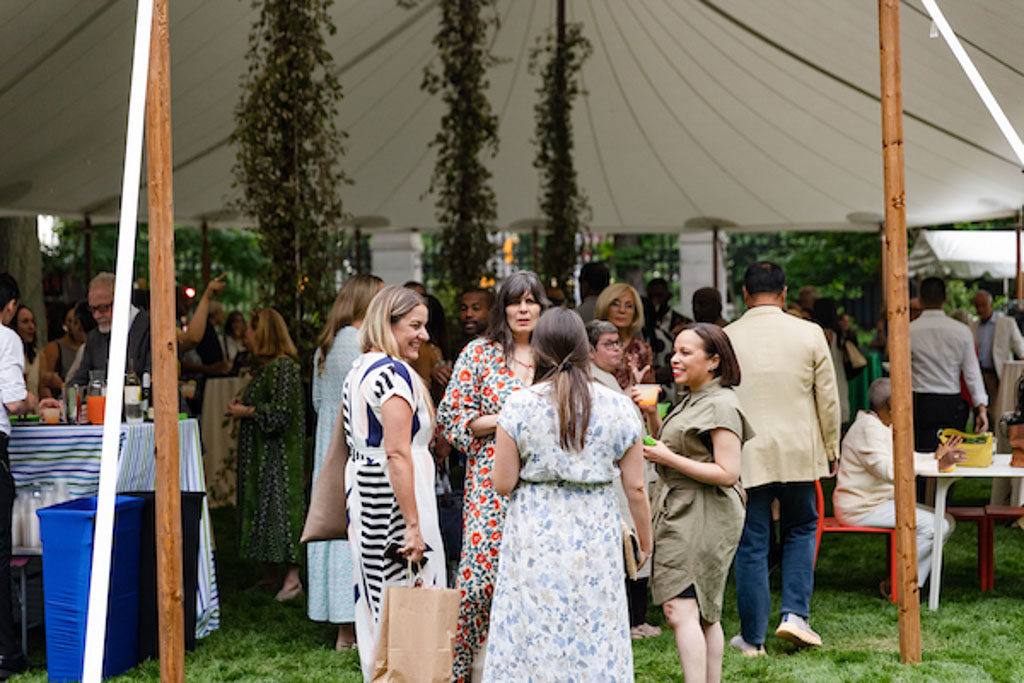 Several people gather beneath a large, white tent festooned with greenery.