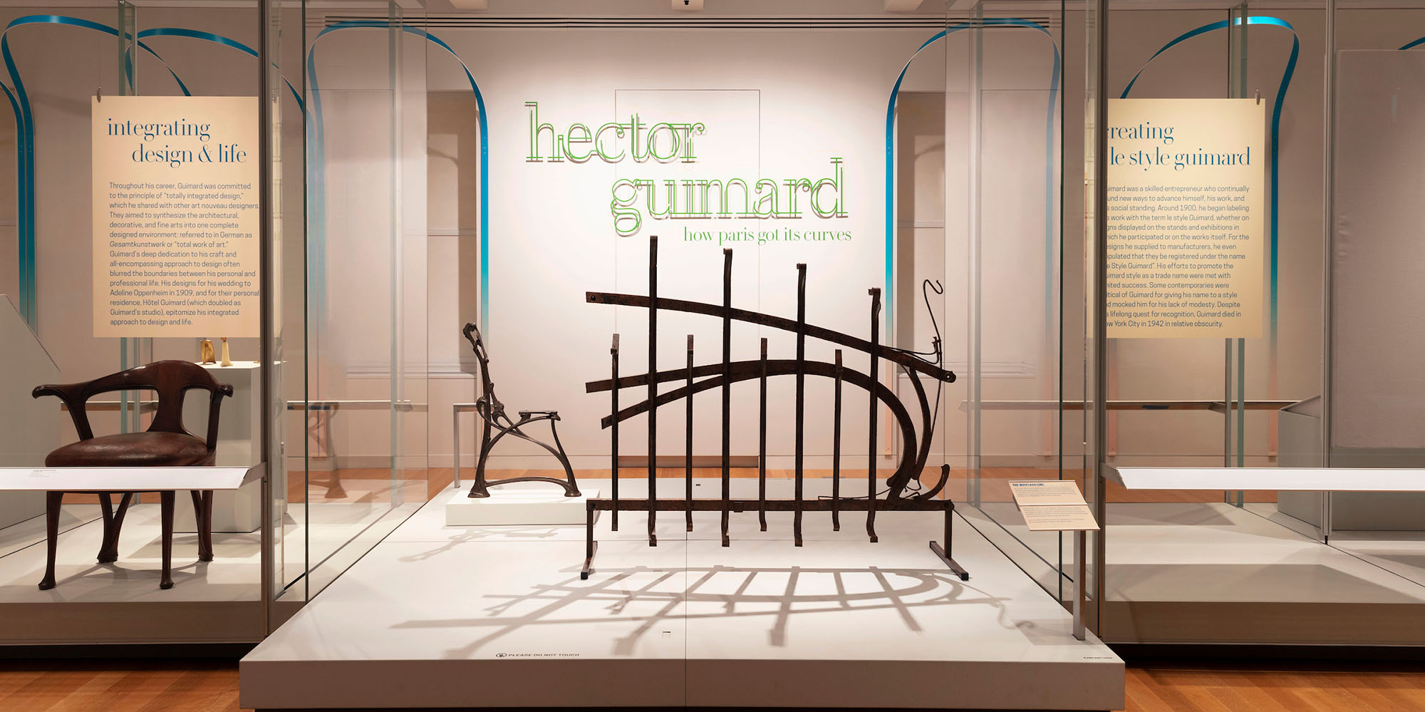 Installation view of "Hector Guimard" exhibition with large iron brackets on display in center platform, alongside an armchair in a glass vitrine.