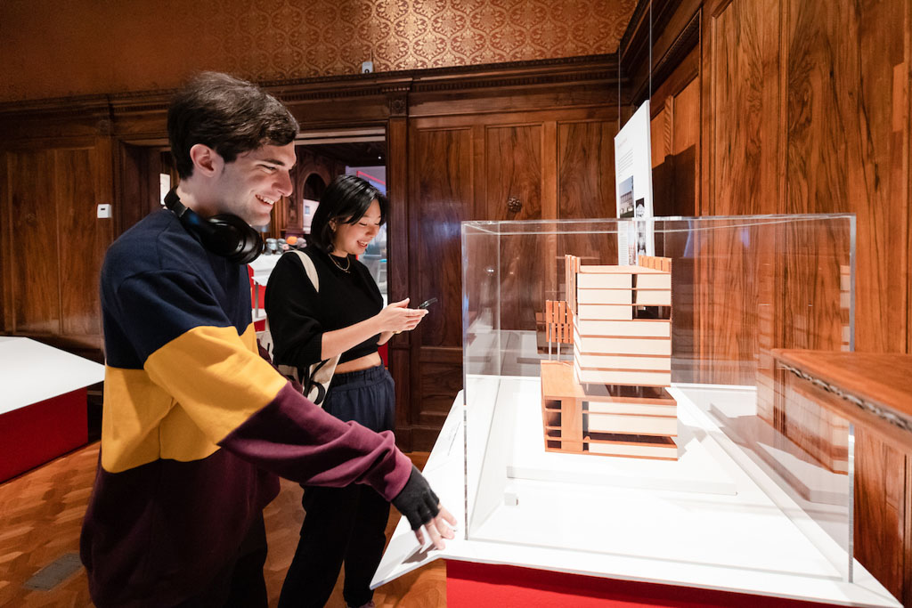 Two people smile as they look at an architectural model in a glass case.