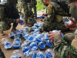 A group of soldiers in army fatigues crouch down to grab from a pile of clear and blue plastic balls.