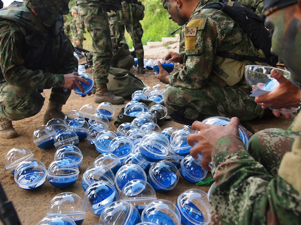 A group of soldiers in army fatigues crouch down to grab from a pile of clear and blue plastic balls.