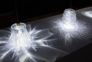Two glass vessels lit from above causing dramatic and intricate patterns of light and shadow to be cast around them.