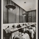 A black and white photograph of an elegant dining room with hanging curtains on the walls dotted with tiny lights.