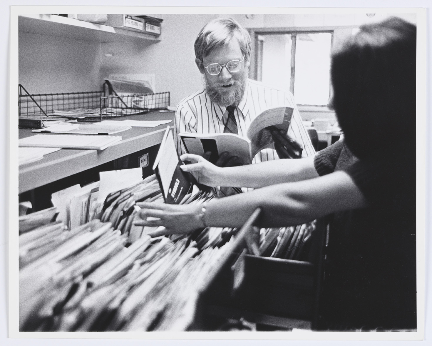 Two people explore the top drawers of an open file cabinet.