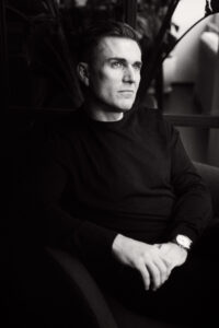 A highly saturated black and white headshot image of a man seated and looking off camera.