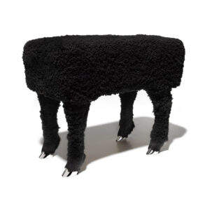 A rectangular stool covered with furry black fabric with four legs, at the bottom of which are silver animal hooves.