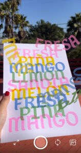 A person holds a sheet of paper with pastel-colored words covering the page, which seemingly appear to leave the page and hover over it.