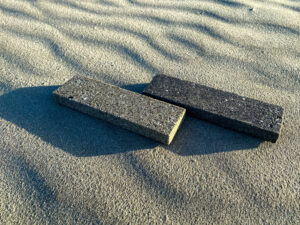 Two rectangular tiles lay diagonally on sand casting long shadows.