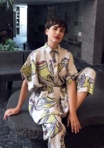 A woman wears a jumpsuit with white and yellow designs, sitting on a black table.