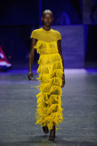 A runway model wears a bright yellow frilly dress.
