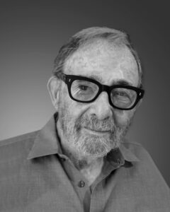 Headshot portrait of a man wearing thick black glasses and a button up collared shirt.