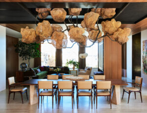 A large rectangular dining room table sits on the foreground in a wide interior under a complex hanging sculpture.