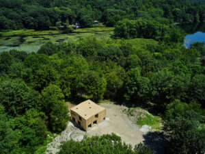 An aerial photograph of a square wooden building surrounded by luscious green forest.