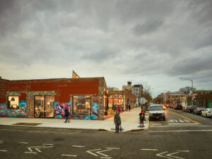 The corner of a brick building decorated with colorful graffiti with dramatic grey clouds above.