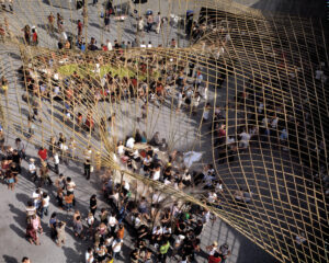 A photograph looking downward on many people gathered under a large golden yellow wire structure.