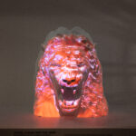 A model of a snarling lion's head, projected with bright orange light and overlapping, barely legible white handwriting.