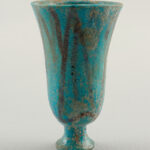 A thick, bell-shaped ceramic cup, its vibrant blue surface striped with dull brown and pockmarked with age.