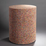 A cylindrical stool covered on all sides with a completely smooth layer of rainbow sprinkles.