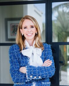 A headshot of a woman wearing a textured blue jacket and white shirt with oversize bow.