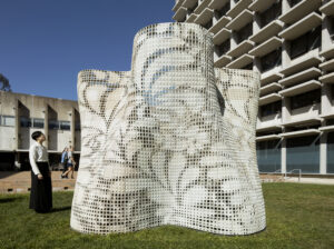 A white sculpture made of mesh-like material that displays patterns of leaves on its surface.