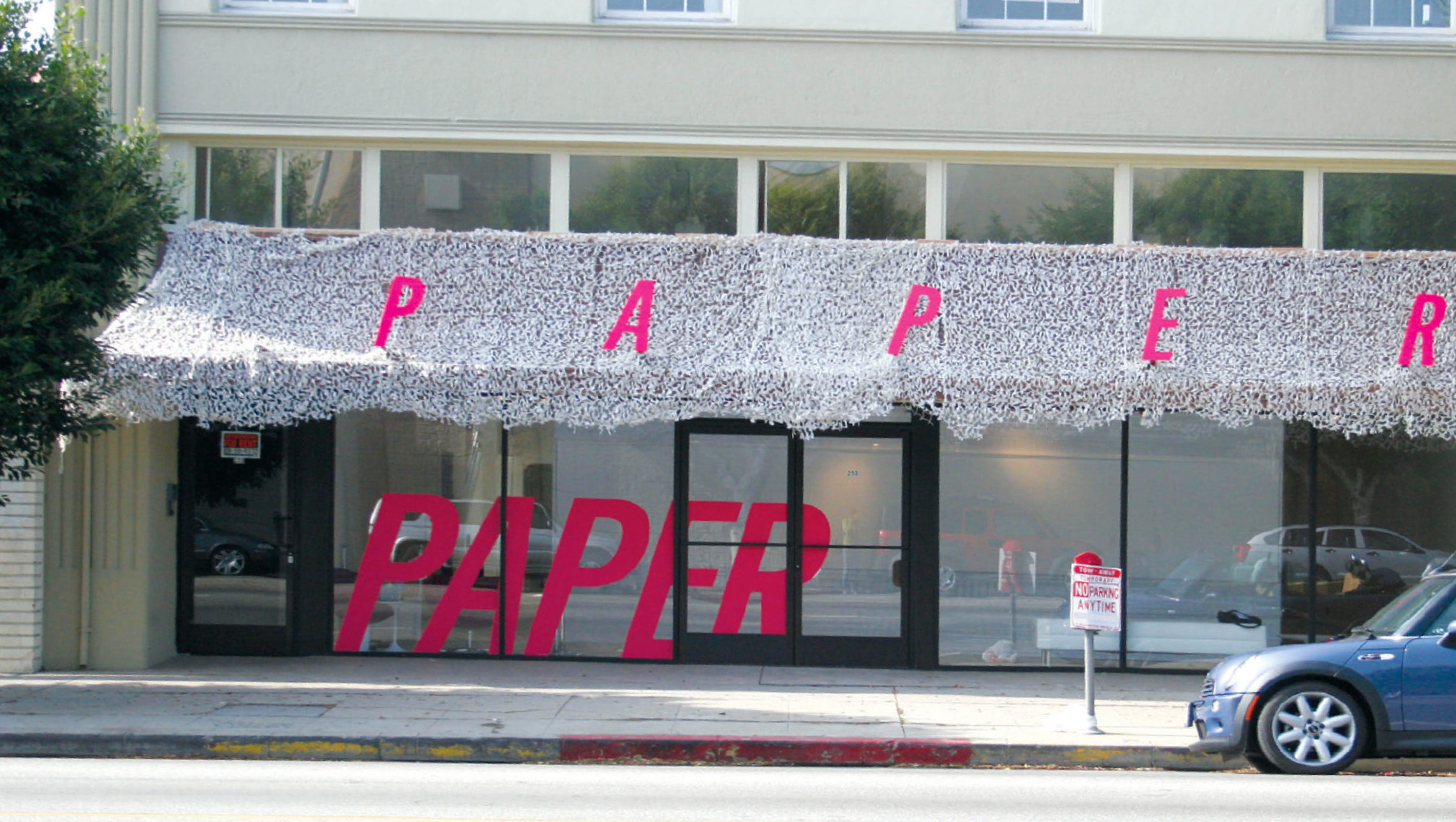 Photograph of a building facade with the word [PAPER] in hot pink capital letters splashed across its awning and windows.
