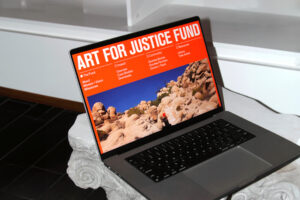 A laptop showing the homepage of the Art for Justice Fund perched on top of a sculpture of an ionic column.