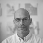A black and white photo of a person wearing light rimmed glasses and a white collared shirt.