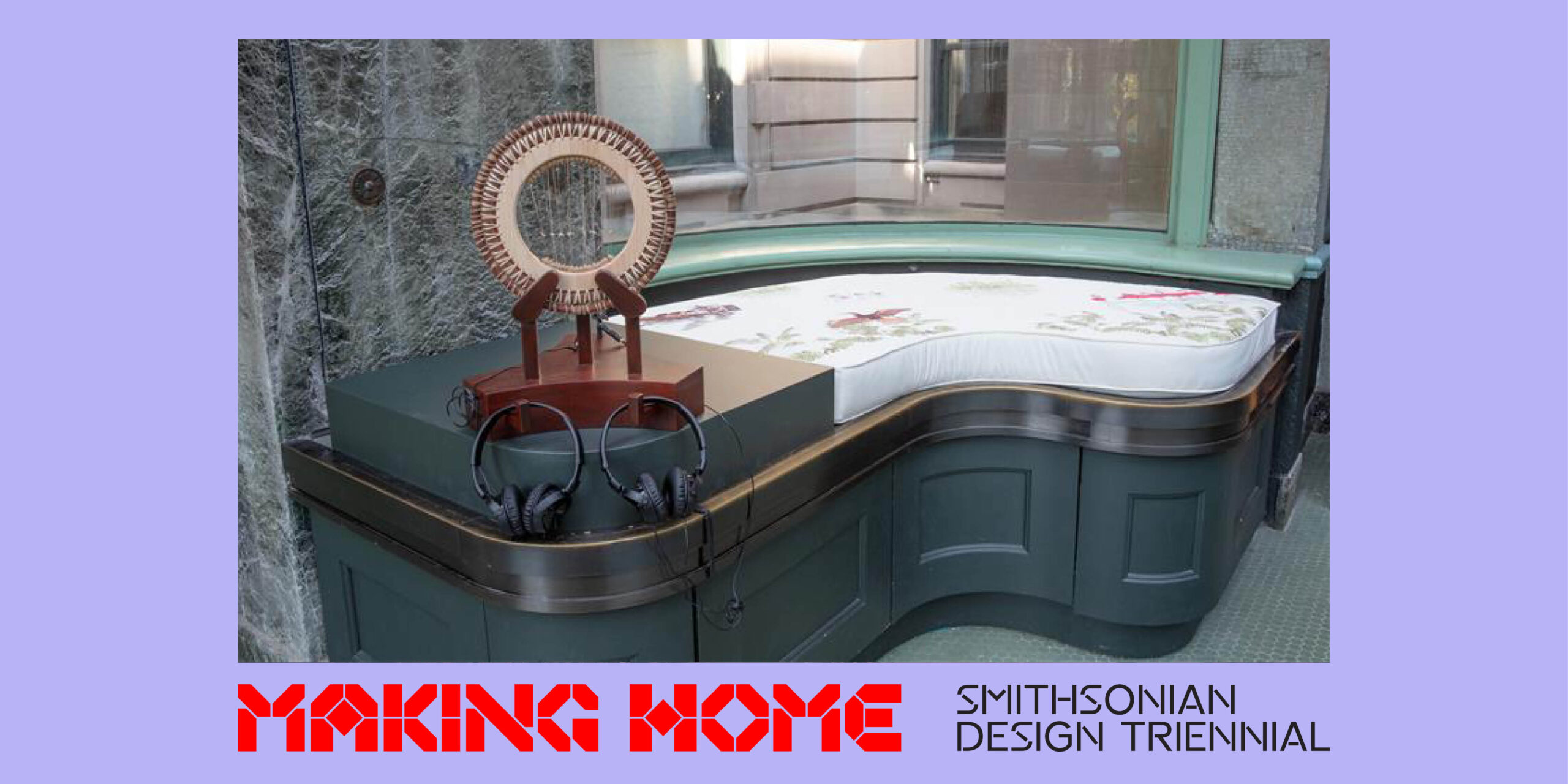 A low bench sits in front of a wall of windows. A circular art object is placed next to the bench, with two pairs of headphones.