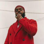 Person in red coat holding hand by chin and looking down.