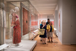Visitors navigating a gallery with a white cane and sighted guide. 