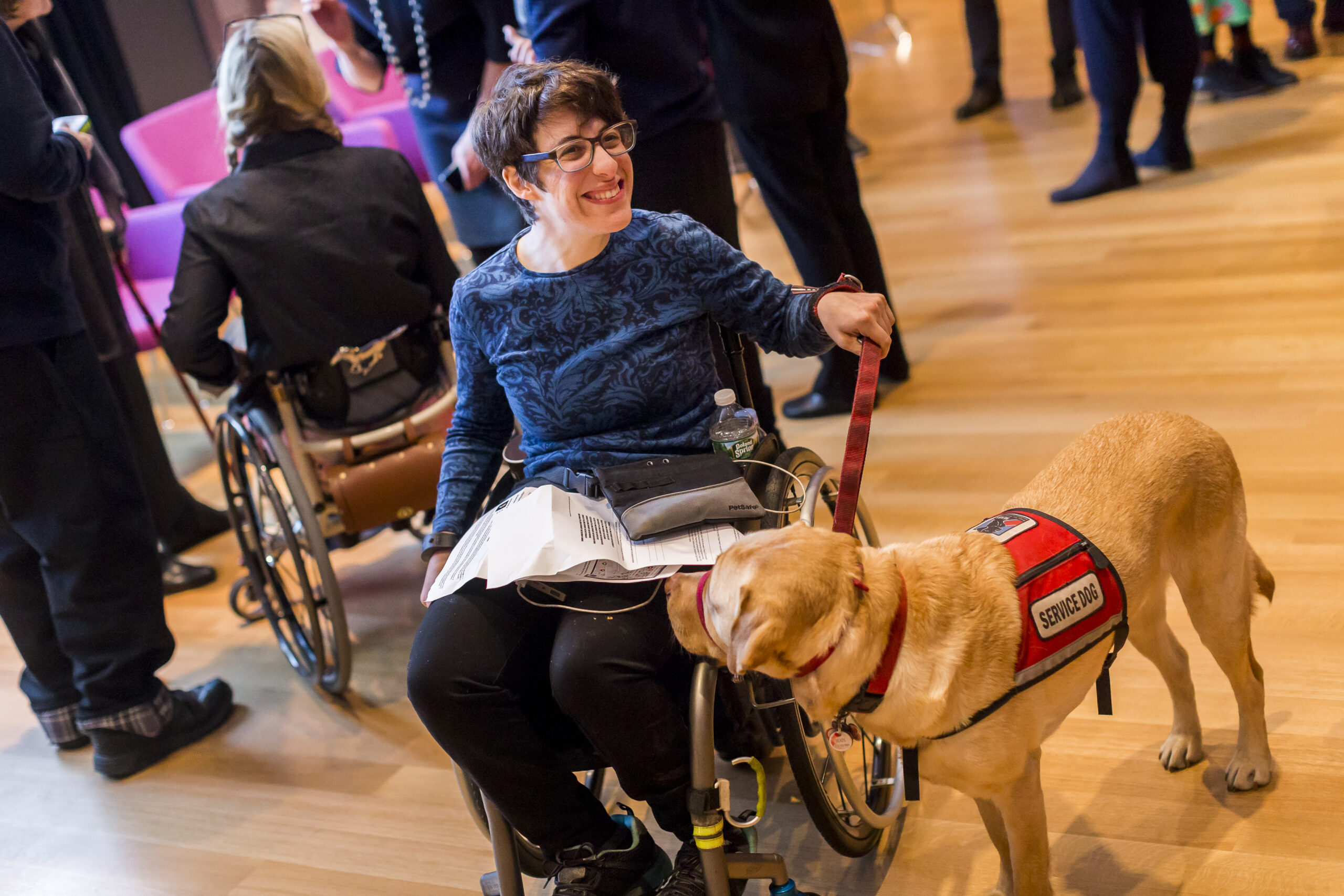 Smiling person using a wheelchair holding the leash of their service dog