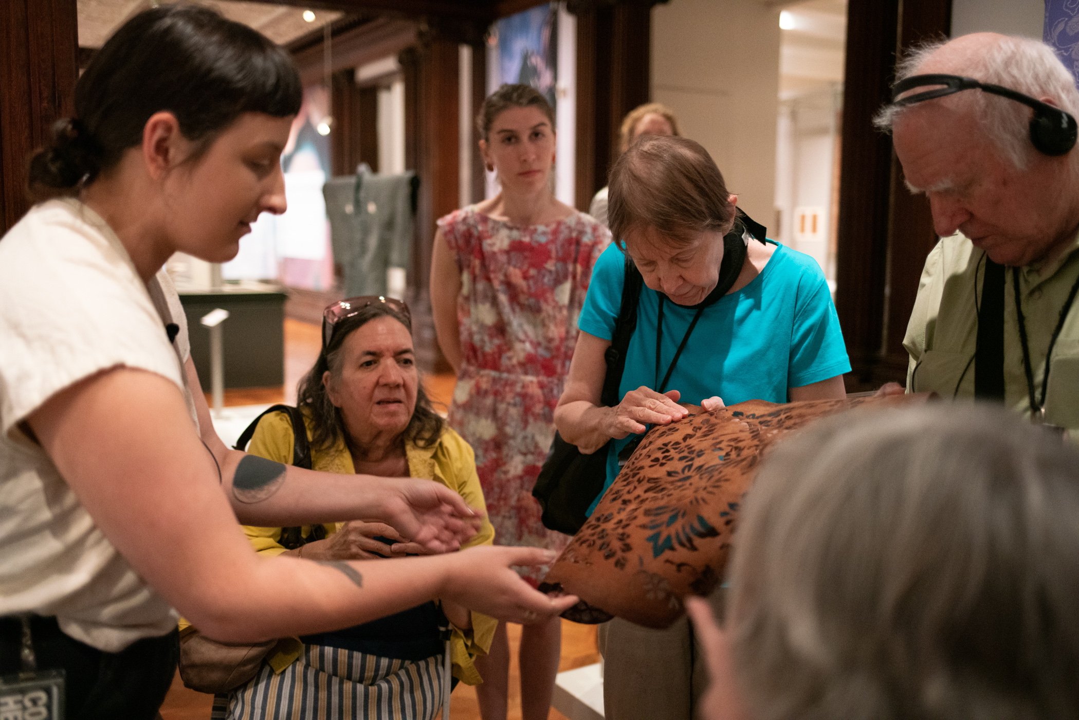 Visitors feeling the texture of a carved leather touch object in a gallery.