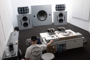 Man in a T-shirt and baseball cap adjusts the tuning on an elaborate sound system.