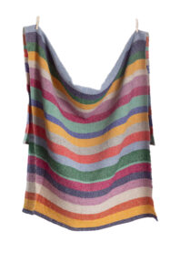 A blanket-sized cloth filled with earthtone horizontal stripes of blue, yellow, green, orange, and pink hangs from clothespins.